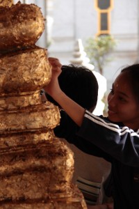 Apposer une feuille d'or sur la statue de Bouddha, en guise d'offrande: un geste habituel pour les bouddhistes en Thaïlande.